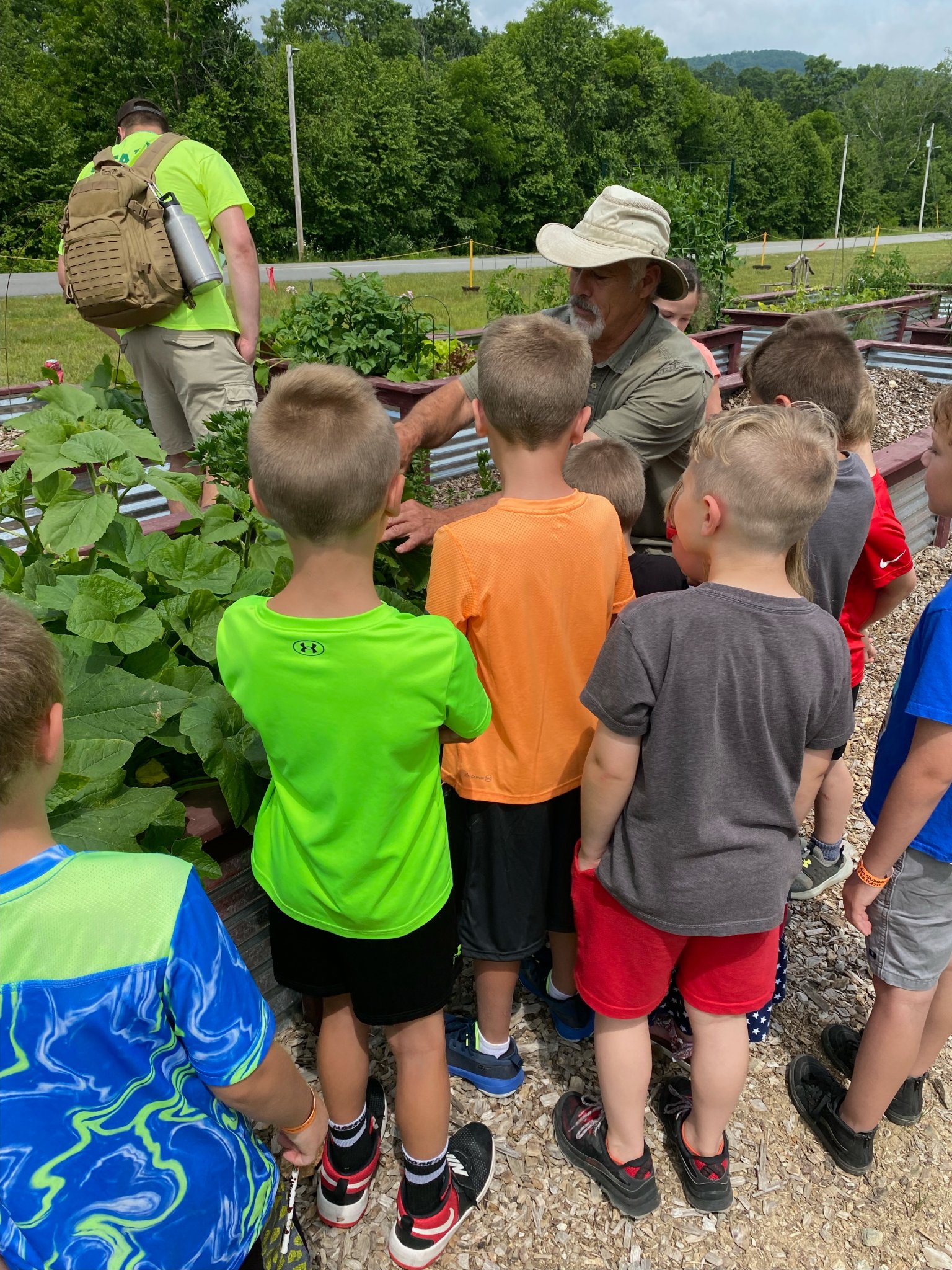 Children gather to view a farmer working with plants.